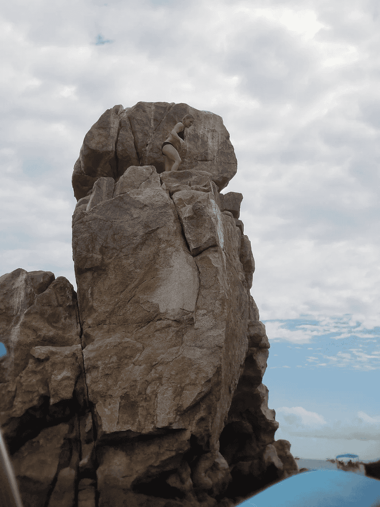 Climber scaling large rock formation at outdoor adventure site for rock climbing.
