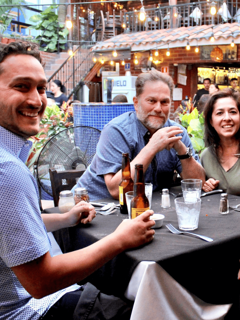 Happy people enjoying drinks at outdoor restaurant with string lights and brick setting.