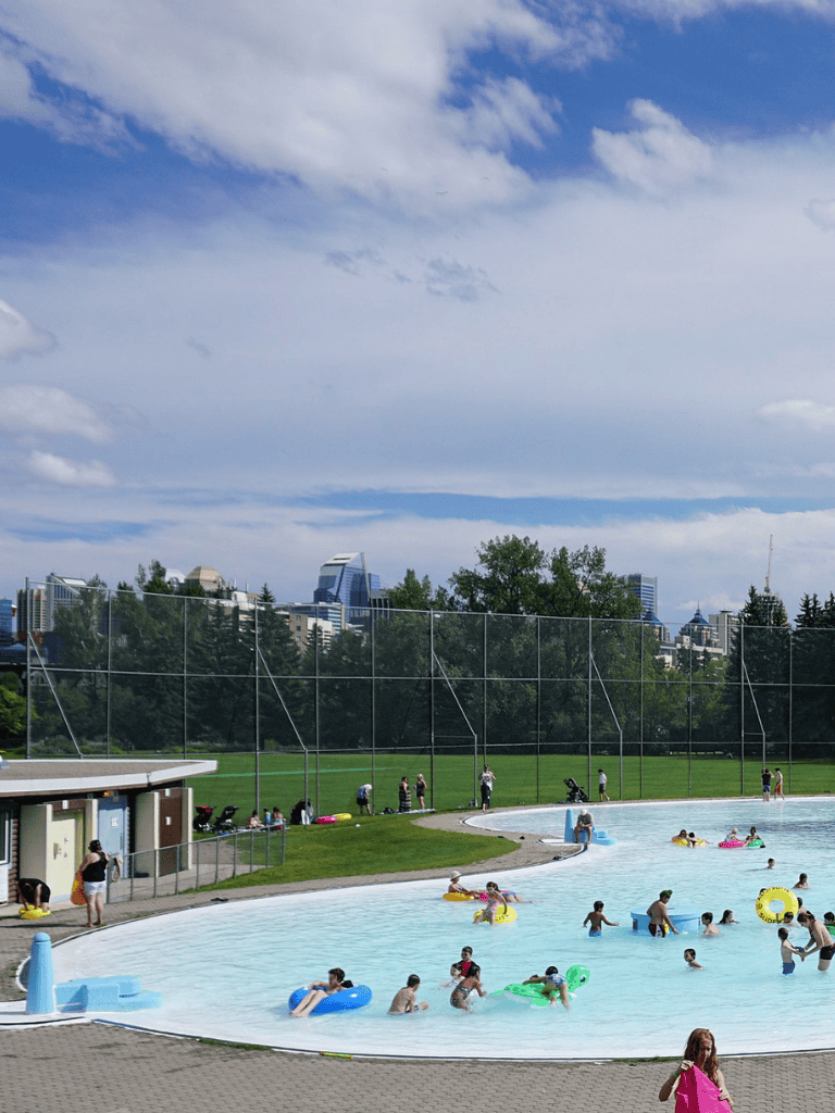 Swimming pool with children playing and an urban skyline in the background.