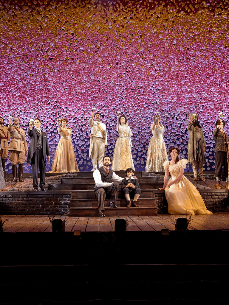 1. Diverse cast performing a theatrical production with a floral backdrop on stage.
