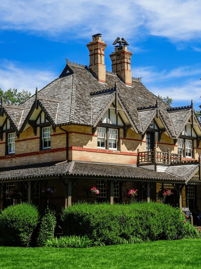 Charming Tudor-style house with lush garden and vibrant hanging flowers, under a bright blue sky.