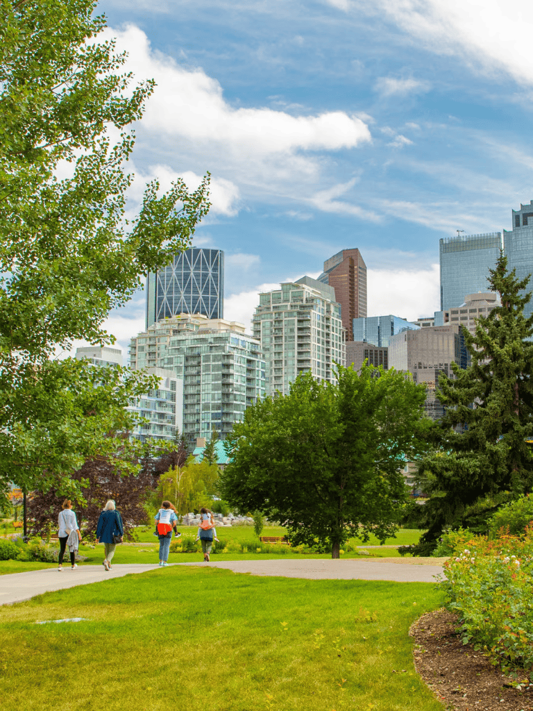 Vibrant urban park with city skyline, green trees, and people walking on pathway.