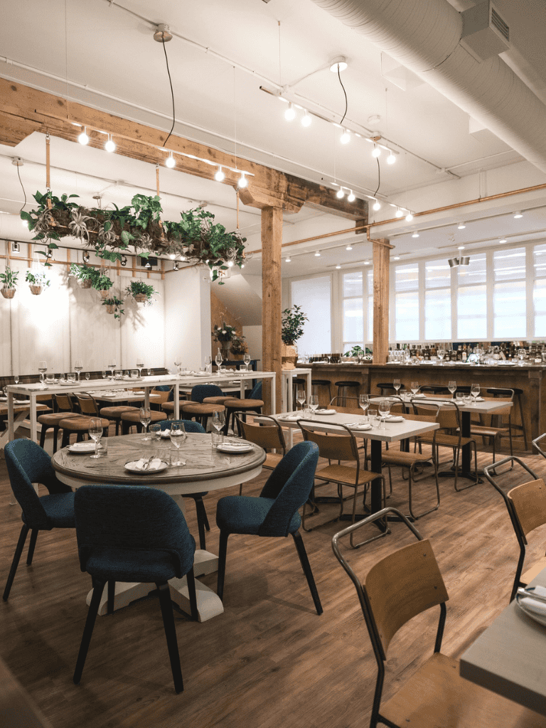 Indoor dining setup with wooden accents, greenery, and modern lighting, perfect for a stylish restaurant experience.