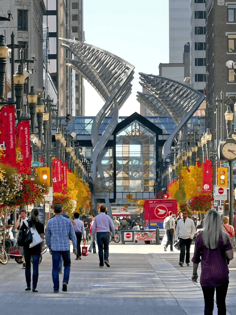 Modern urban street scene with People walking and distinctive architecture, bright fall foliage, and city lights in the background.