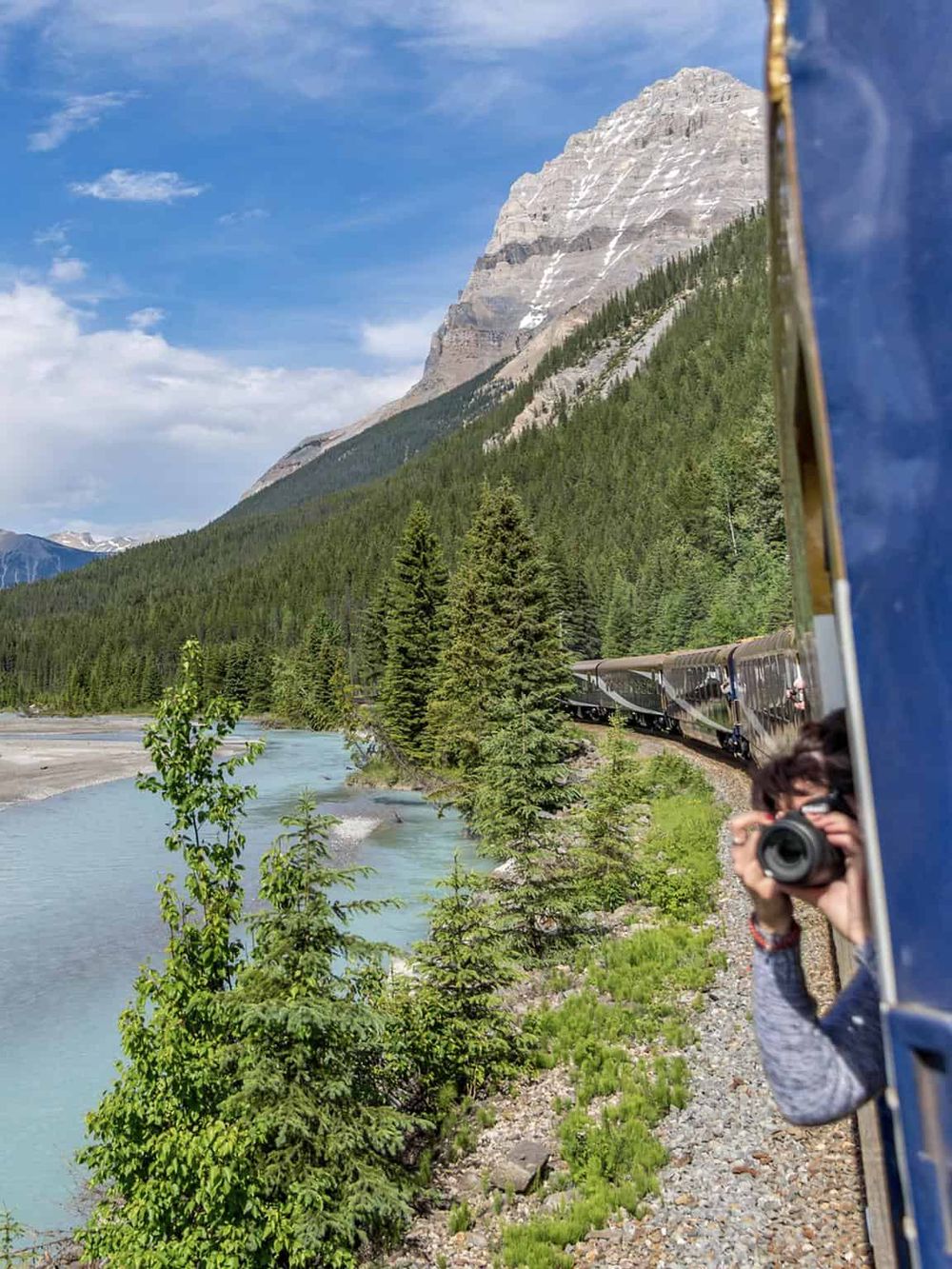 Scenic train journey through lush forests and mountains, capturing nature's beauty with a traveler taking photos.