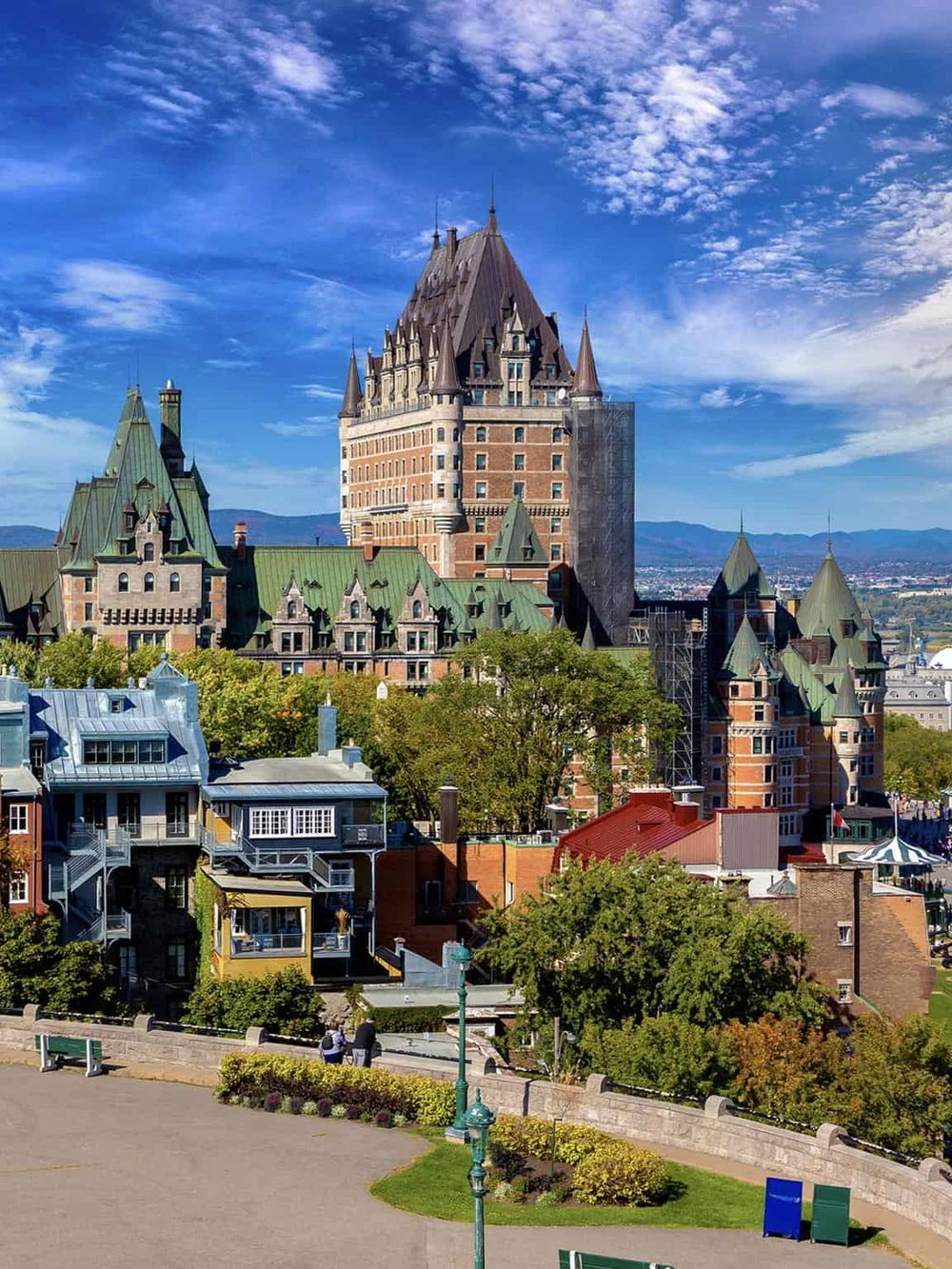 Ancient castle with green-roofed turrets under a blue sky, surrounded by trees and modern buildings.