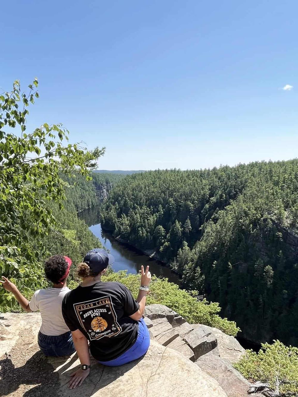 Aerial view of two people enjoying a scenic overlook of a forested canyon and river, perfect for nature exploration and outdoor adventures.