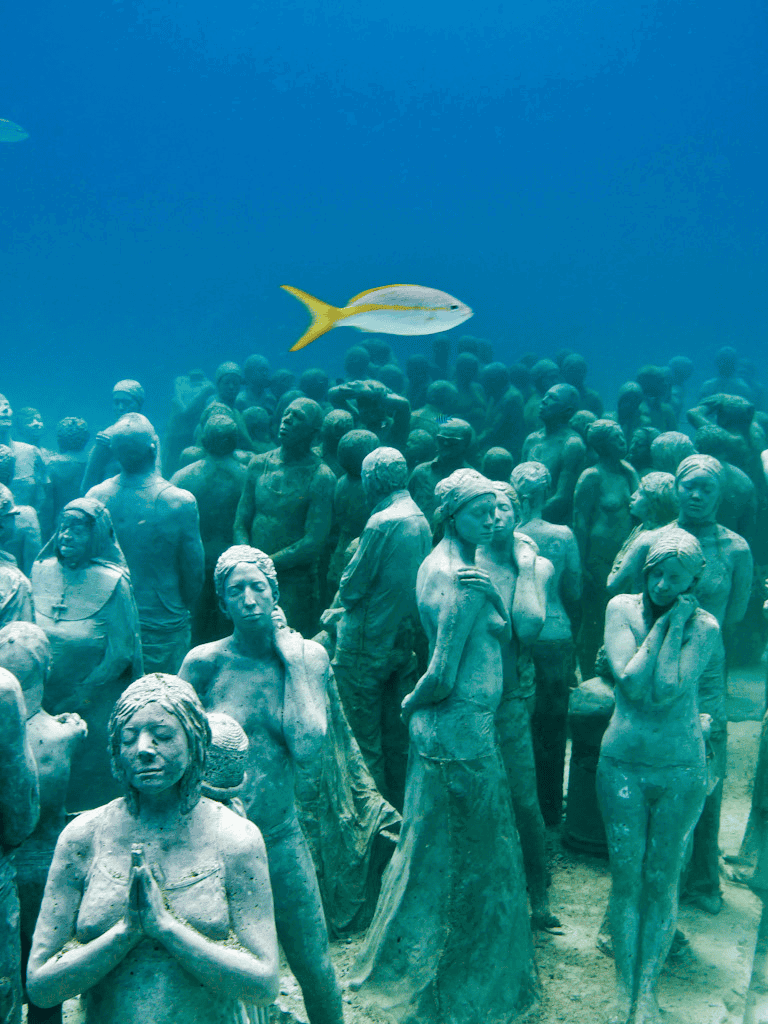 Aquatic sculptures of diverse women with a fish swimming above, under the ocean.