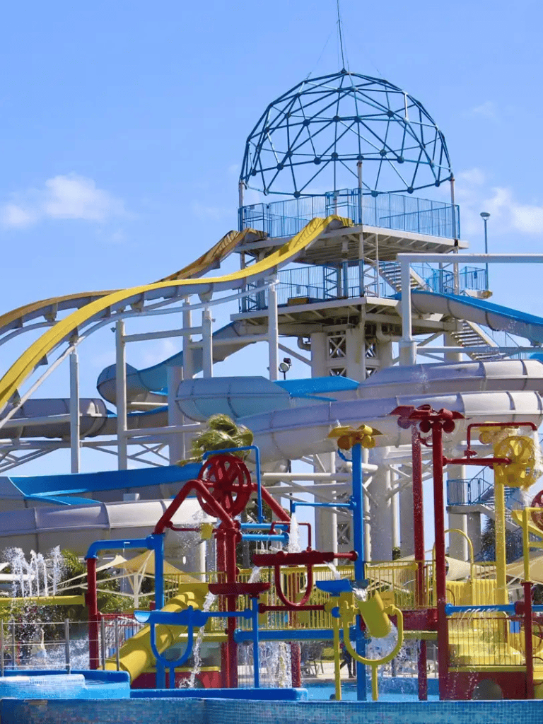 Colorful water park water slides and play structures with a geodesic dome sky background.
