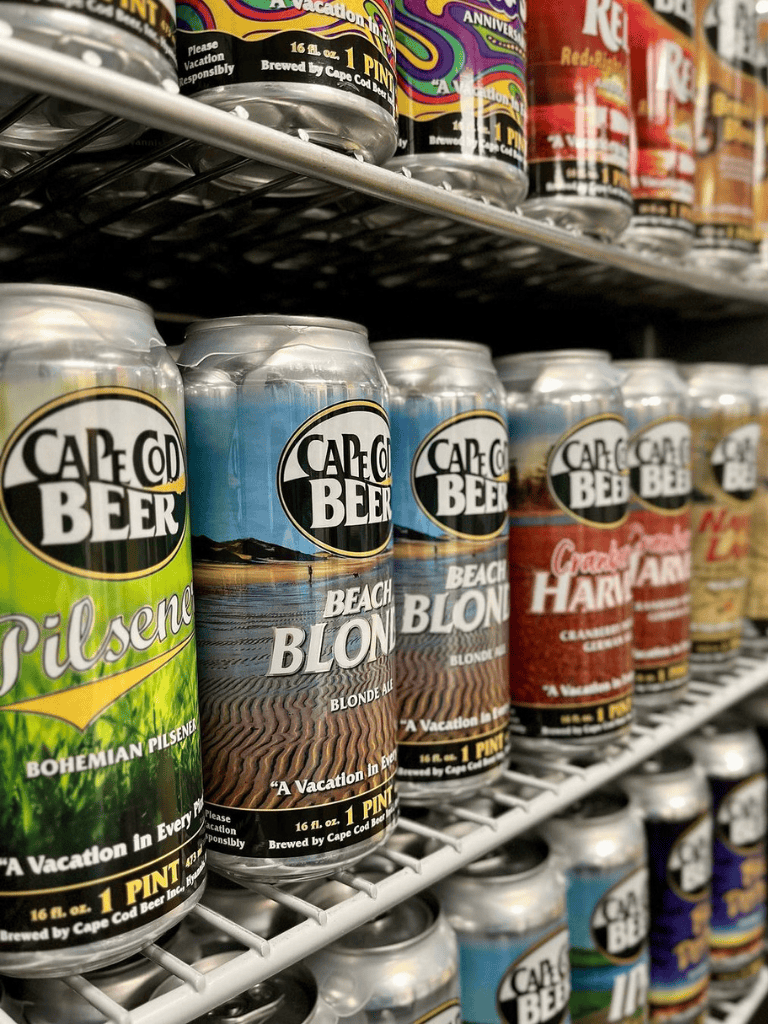 Bright Cape Cod Beer cans featuring beach-themed labels on a store shelf, showcasing local craft beer options.