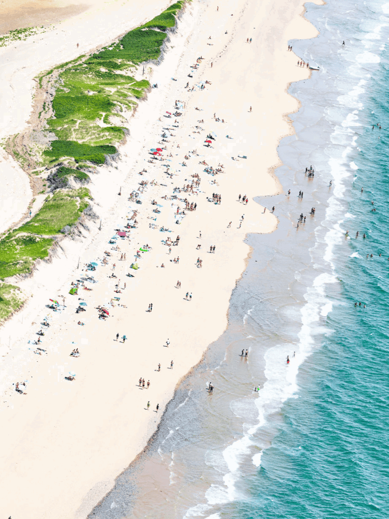 Bright beach scene with people relaxing and playing along sandy shoreline and ocean waves.