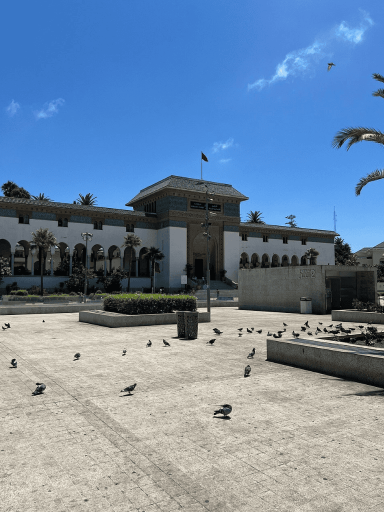 Bright sunny day at historic building with pigeons in public square and blue sky overhead.