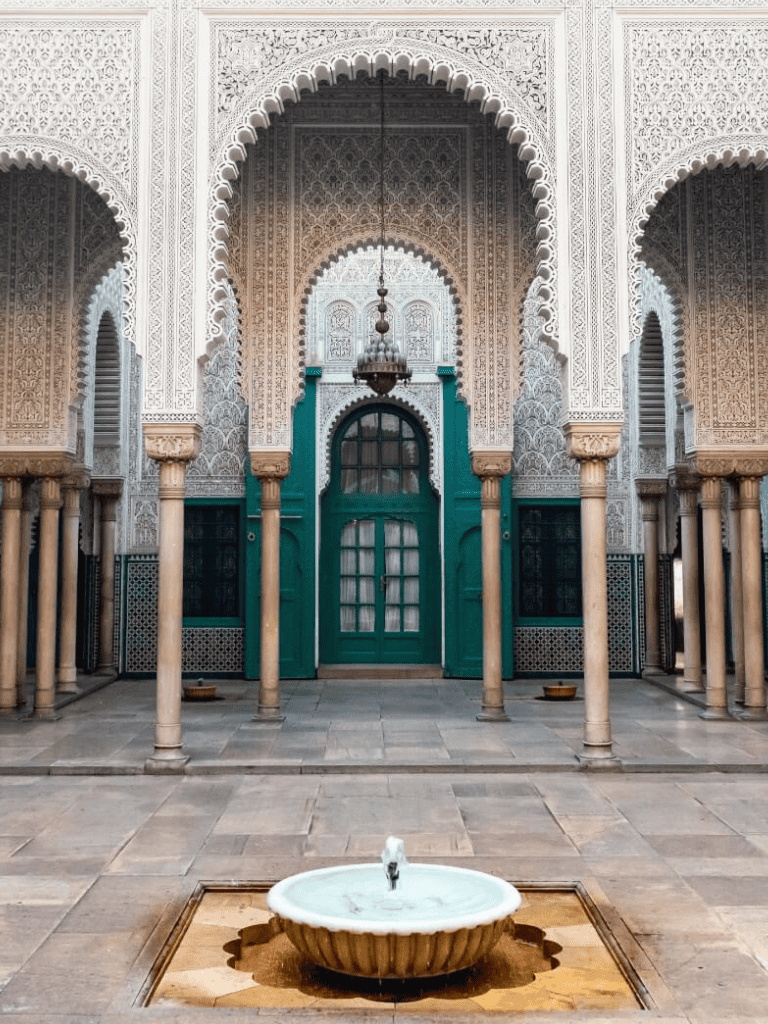 Intricate Moroccan courtyard with ornate arches, columns, and central fountain, showcasing traditional Islamic architecture.