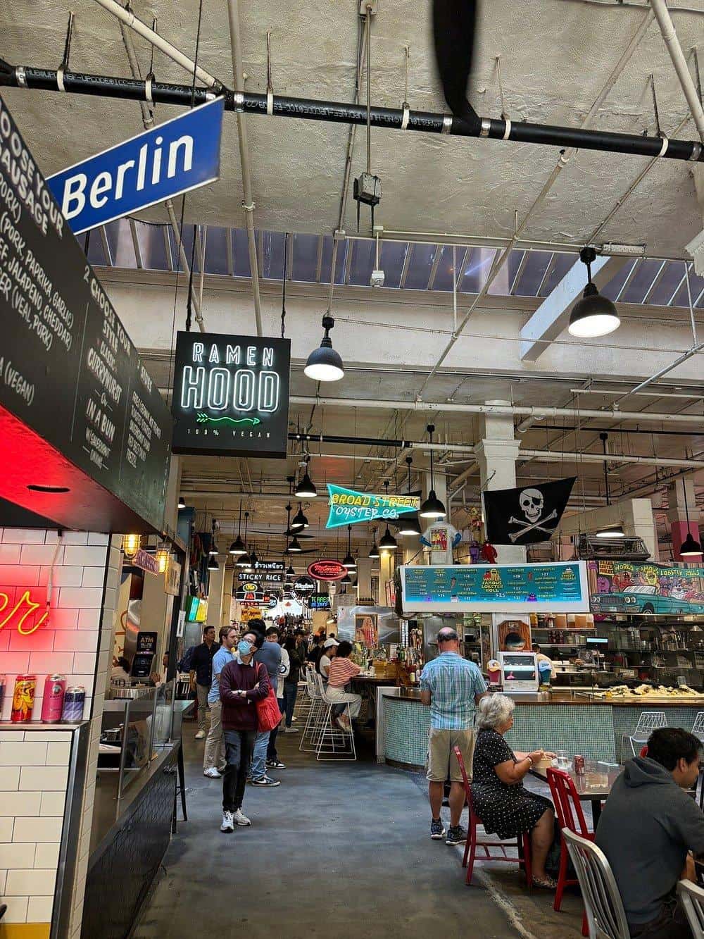 Vibrant indoor market with food stalls, neon signs, and diverse diners, showcasing a lively culinary scene.