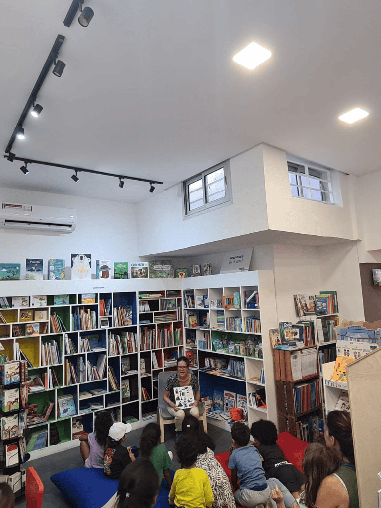 Reading session in a cozy children’s library with kids listening to a storyteller surrounded by books.