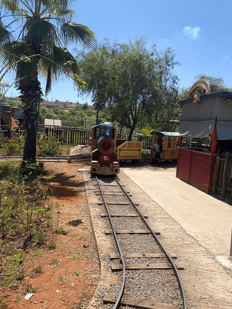 Colorful miniature train on a small outdoor track with trees and blue sky.