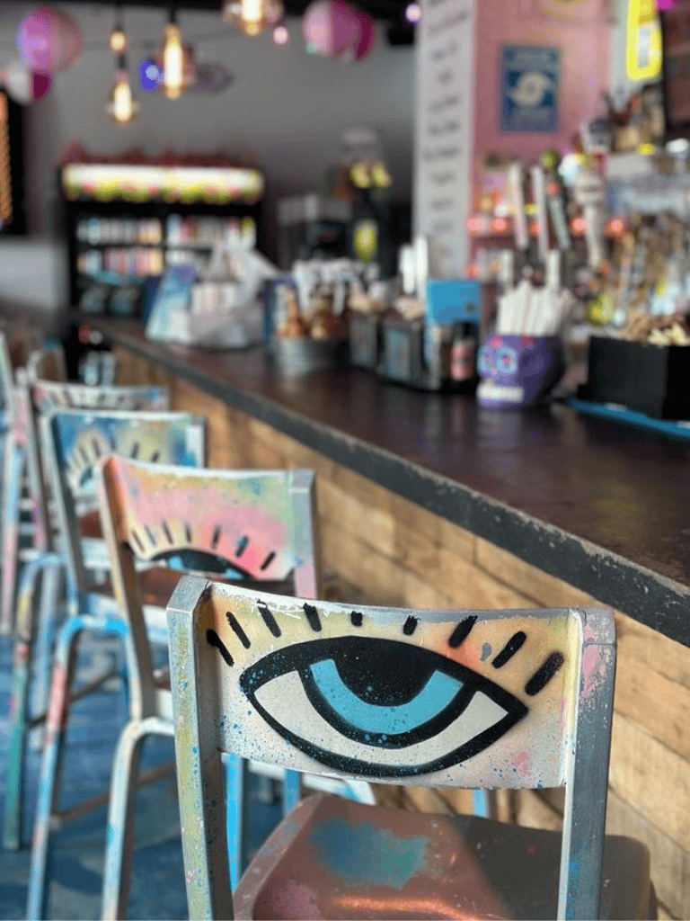 Colorful eye-themed chairs at a vibrant cafe with graffiti art accents.