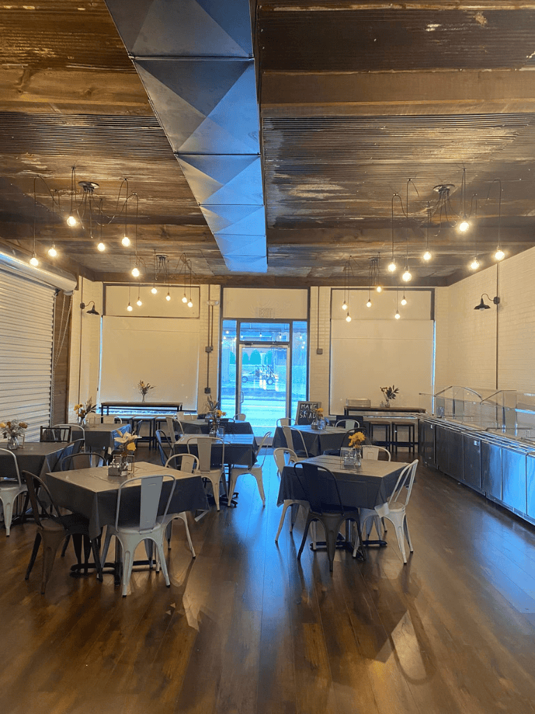 Modern industrial restaurant interior with wooden floors, hanging lights, and tables for dining.