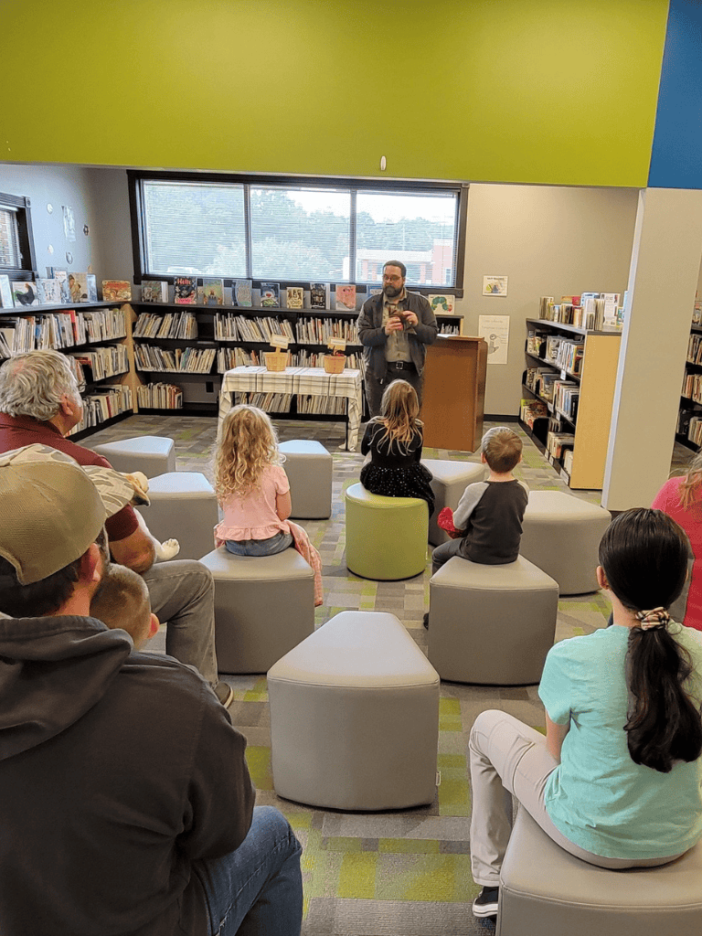 - Modern library reading area with children and adults listening to storyteller.