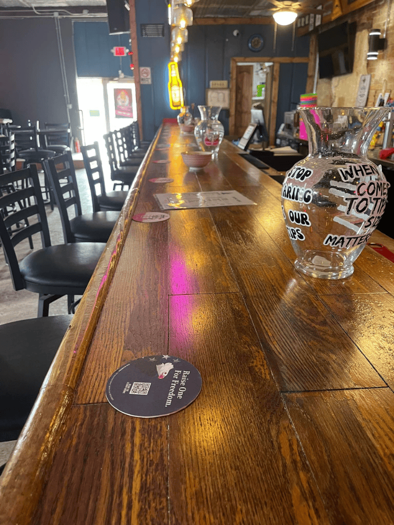 Handcrafted glass water pitcher with inspirational quotes at a rustic bar counter.