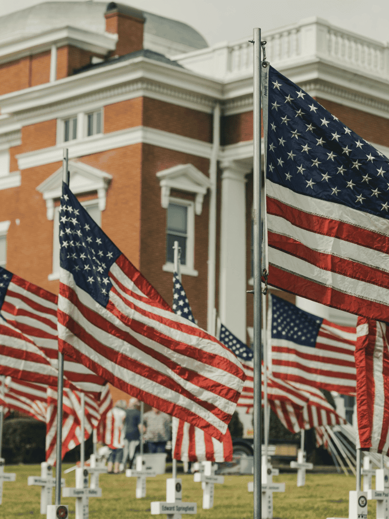 American flags flying outdoors in front of a historic brick building, emphasizing patriotism and national pride.