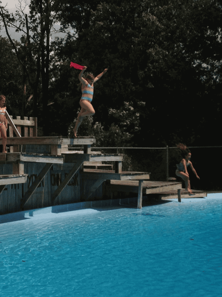 Children jumping into a swimming pool at a summer outdoor water park.