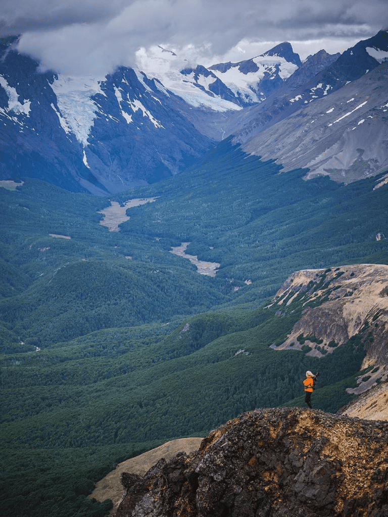 Breathtaking mountain landscape with hiker overlooking green valleys and snow-capped peaks.