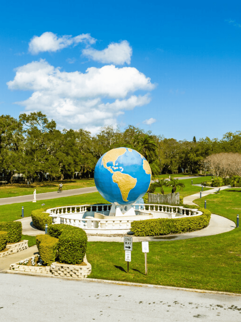 Bright blue sky with white clouds over a large globe sculpture in a park, symbolizing global travel and exploration.