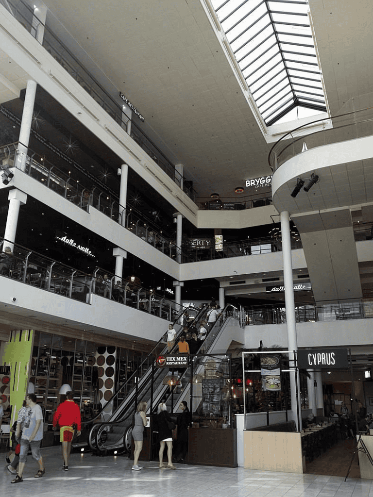 Indoor shopping mall with multiple floors, escalators, and retail stores.