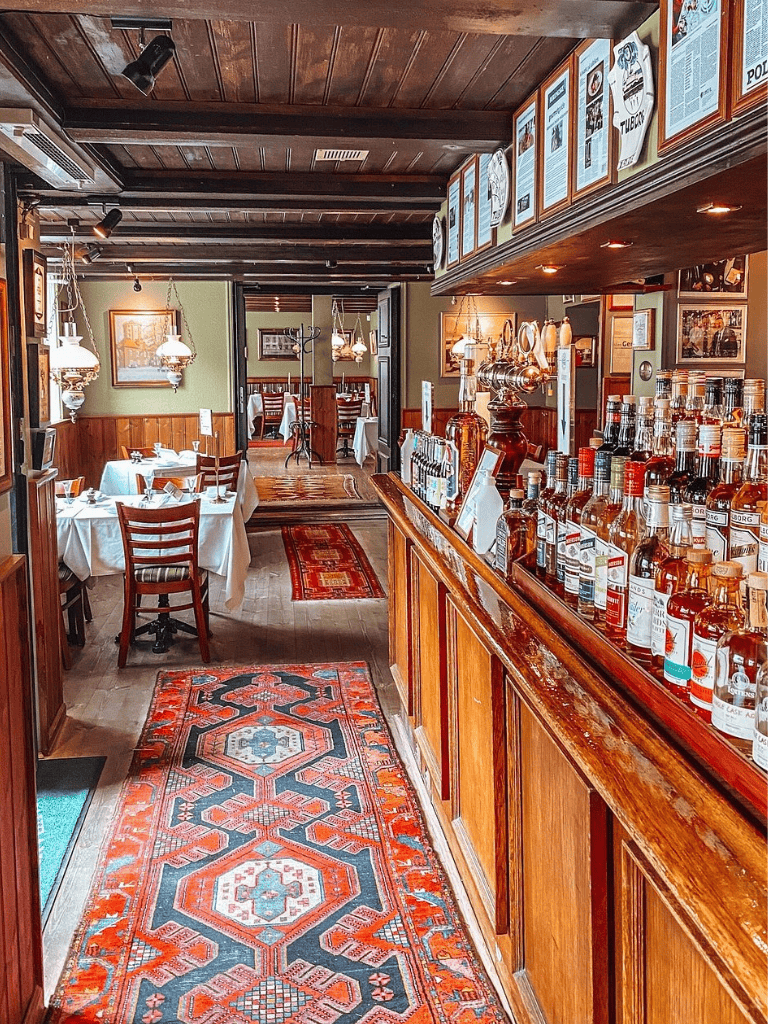 Aisle view of cozy restaurant interior with wooden accents and colorful patterned rug, inviting atmosphere.