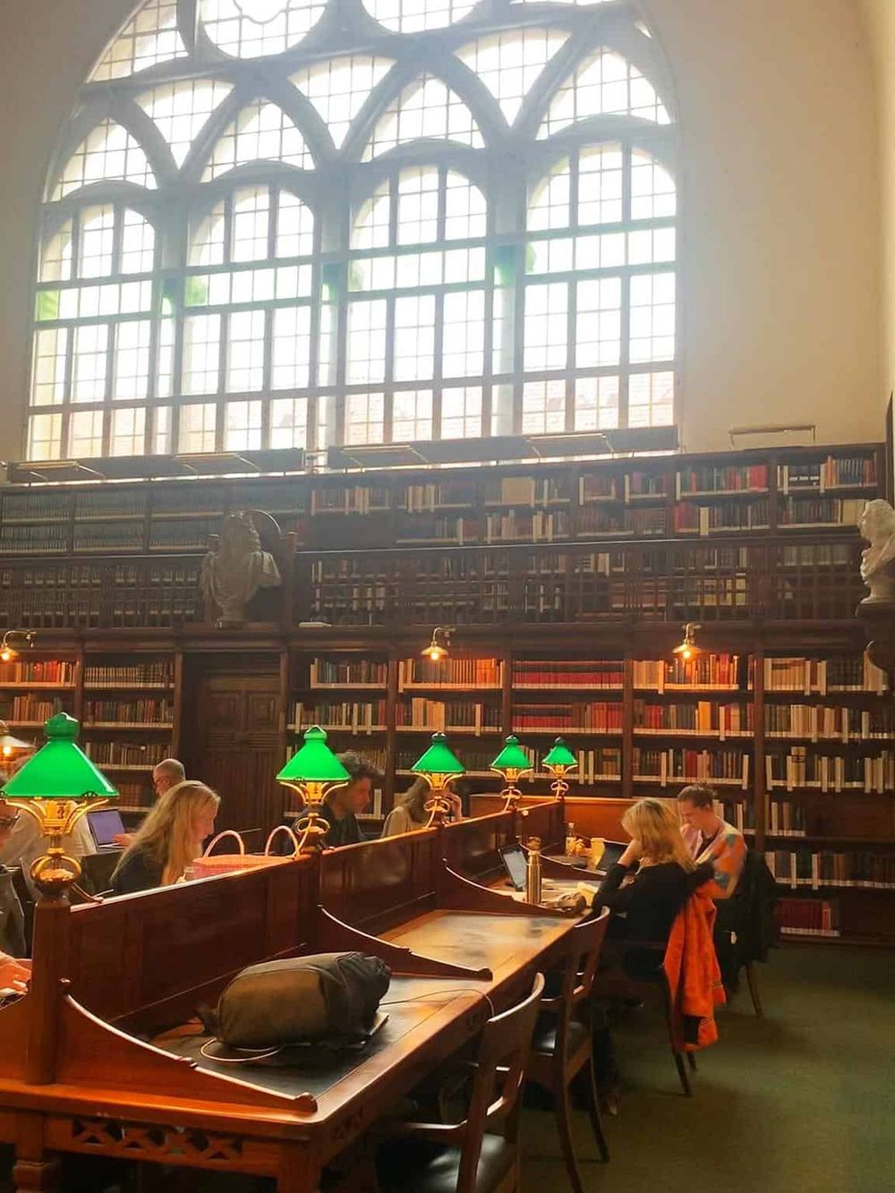 Ancient library with high stained glass windows and people studying at wooden desks, ideal for travel & history enthusiasts.