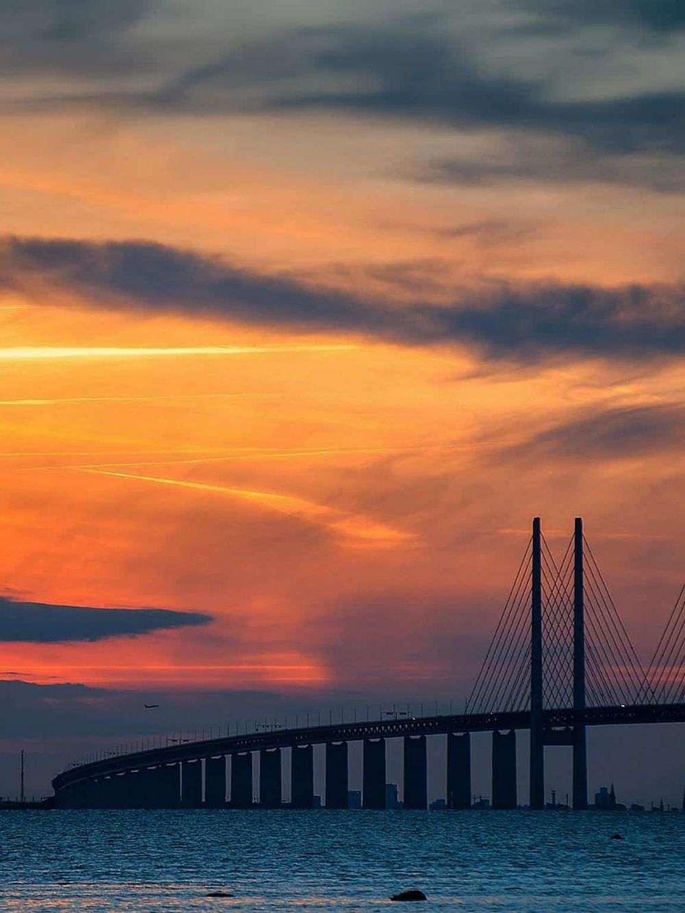 Stunning sunset view over a modern cable-stayed bridge connecting urban areas with scenic water surroundings.