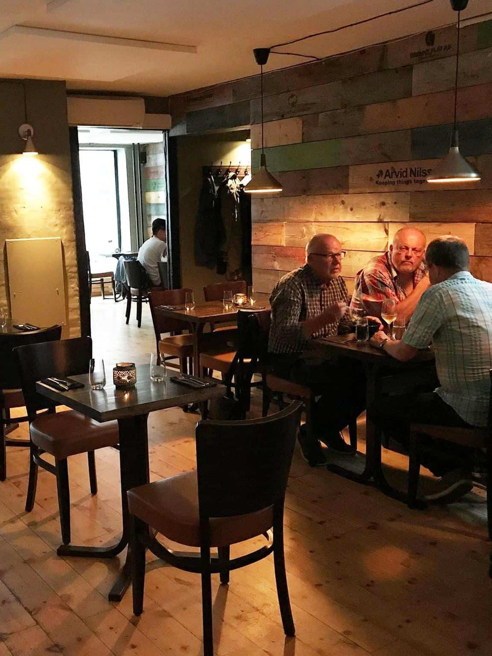 Cozy restaurant interior with wood-paneled walls, dim lighting, and groups of people enjoying meals and drinks.