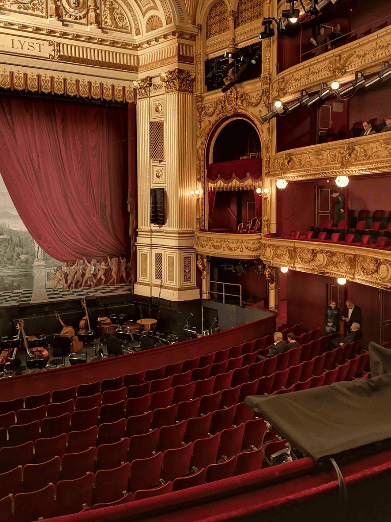 Elegant historic theater interior with plush red seating and ornate gold detailing.