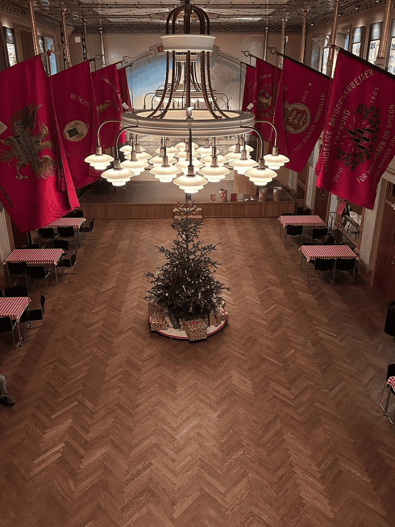 Christmas tree with presents inside a decorated event hall with hanging flags and vintage decor.