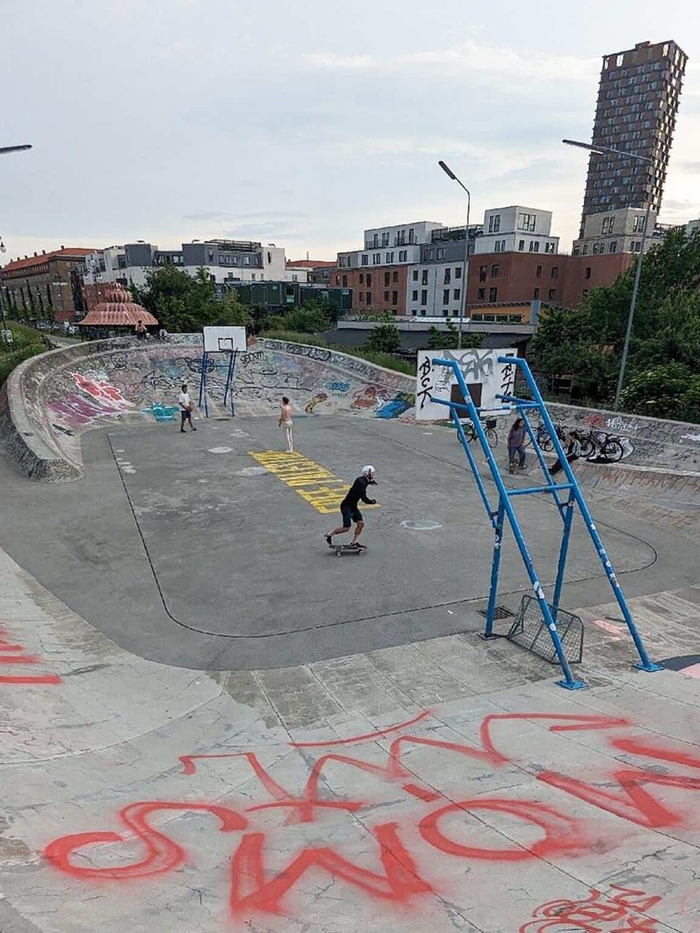 Skateboarding at outdoor skatepark with graffiti, city buildings in background, urban recreation, innovative skate spot.