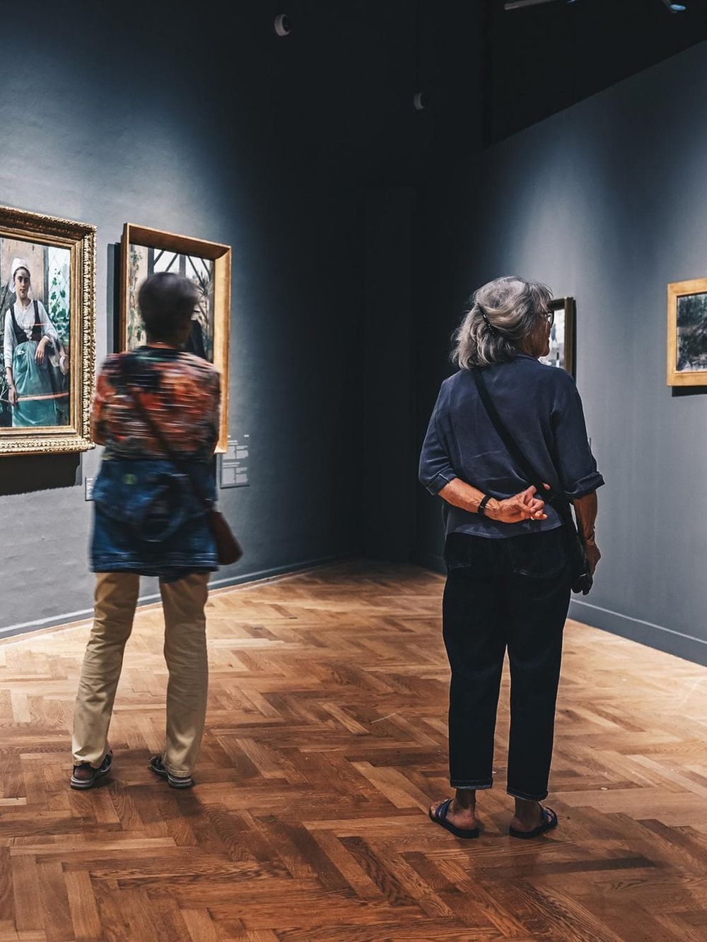 Visitors viewing artwork at an art gallery, exploring paintings in a modern museum setting.