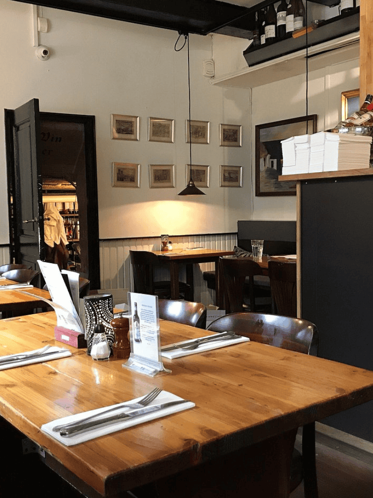 Cozy restaurant interior with wooden tables, framed artwork, and warm lighting, ideal for dining and social gatherings.