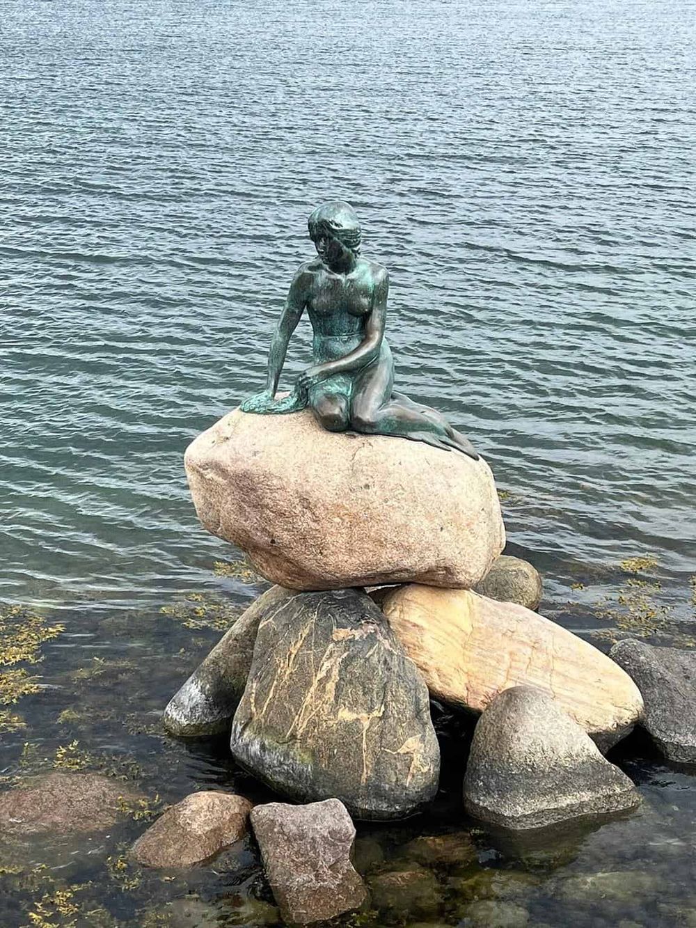 Serene mermaid statue on rocks by the water, showcasing artistic coastal sculpture for travel and outdoor photography.