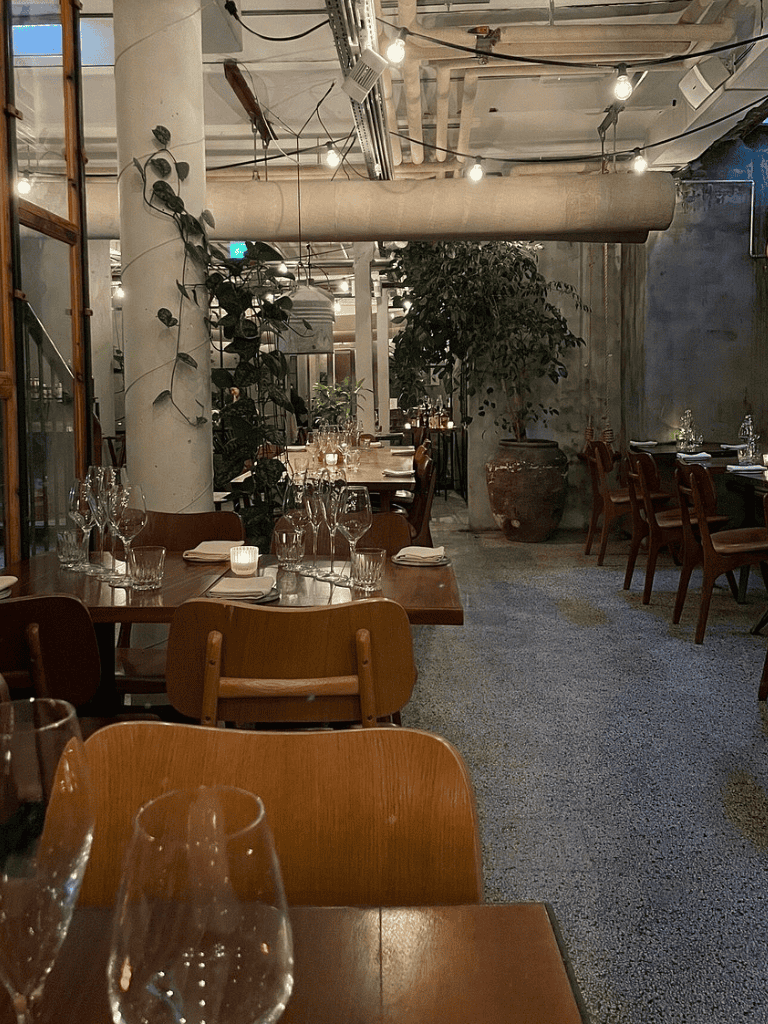 Modern urban restaurant interior with wooden dining tables and decorative plants.
