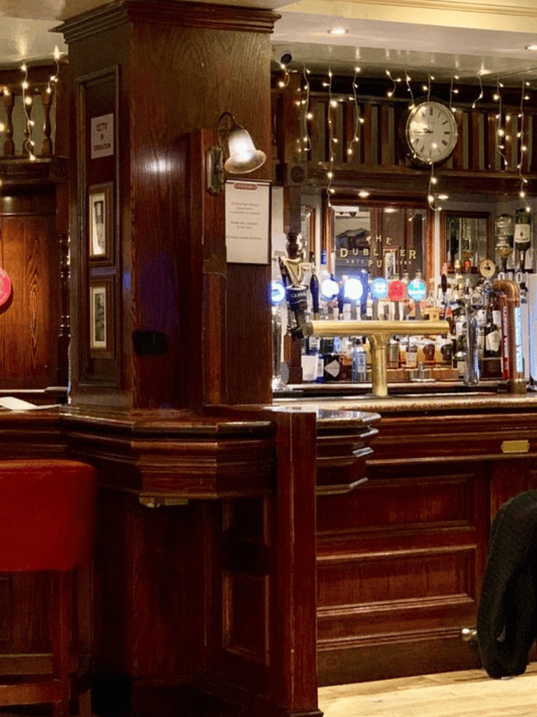 Warm wooden pub interior with bar counter and neon beer signs, cozy lighting with fairy lights, perfect for relaxing with drinks.