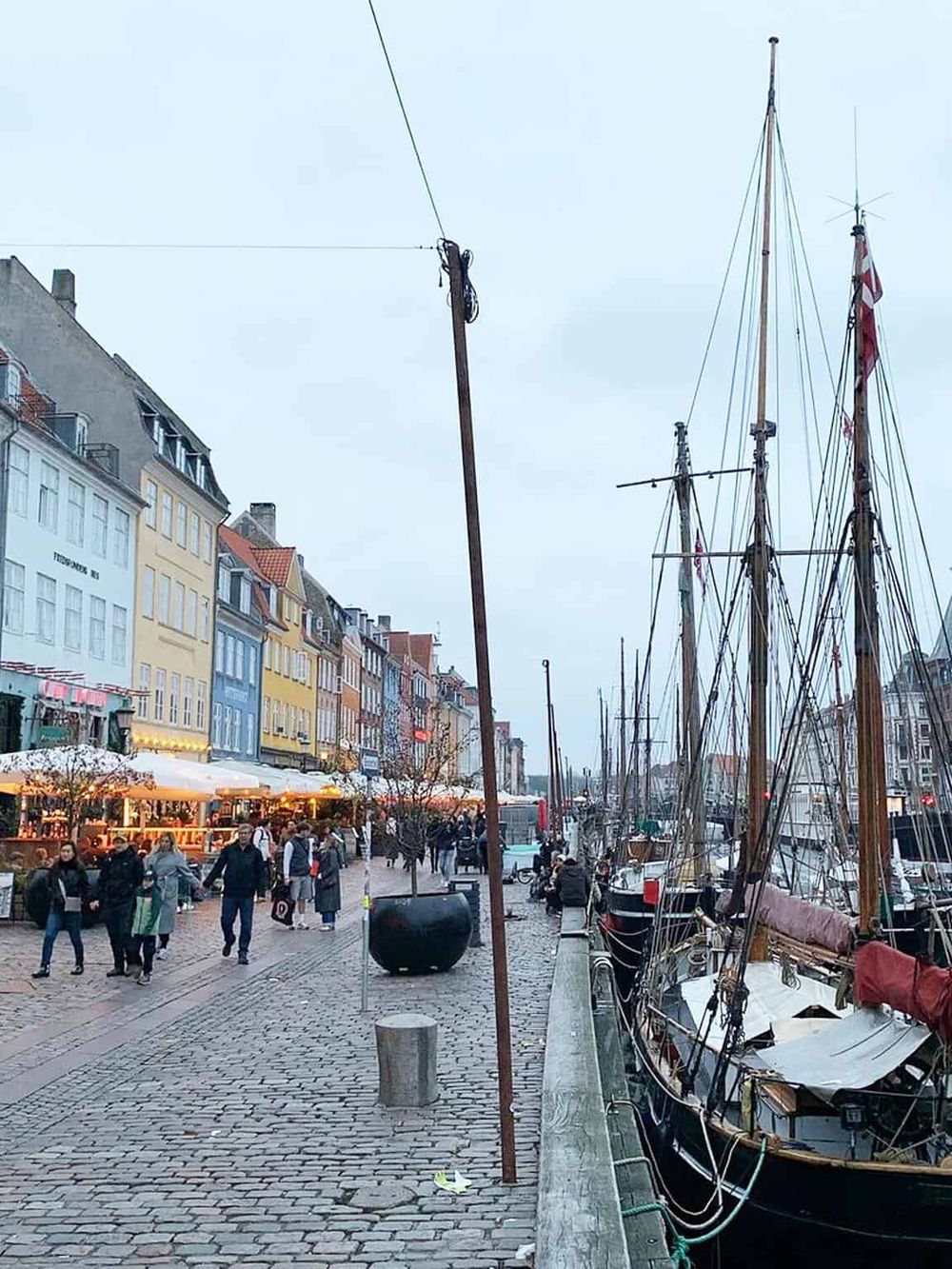 Colorful waterfront street with boats, shops, and pedestrians in Copenhagen, Denmark.