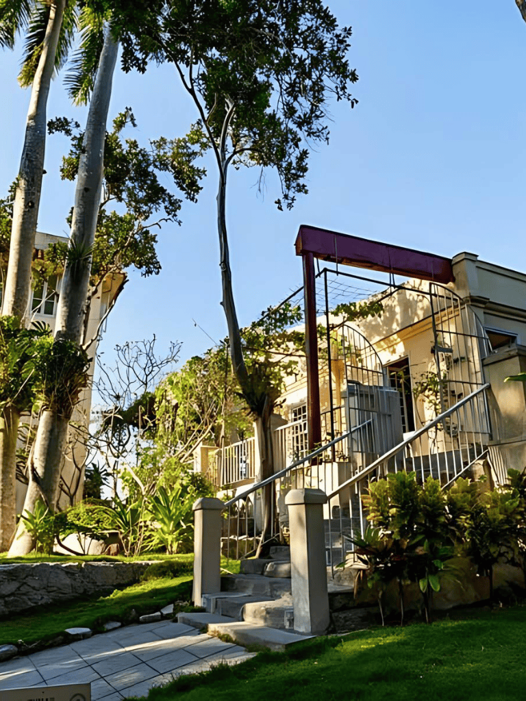 Aerial view of residential building with tropical landscaping and walk-up stairs, sunny sky, lush greenery, Quest For Directions.