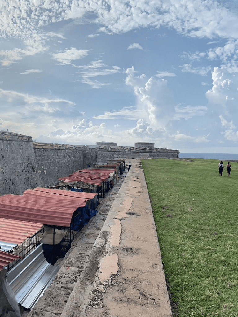 Historic fort wall with market stalls and ocean view under blue sky, sightseeing in Puerto Rico.