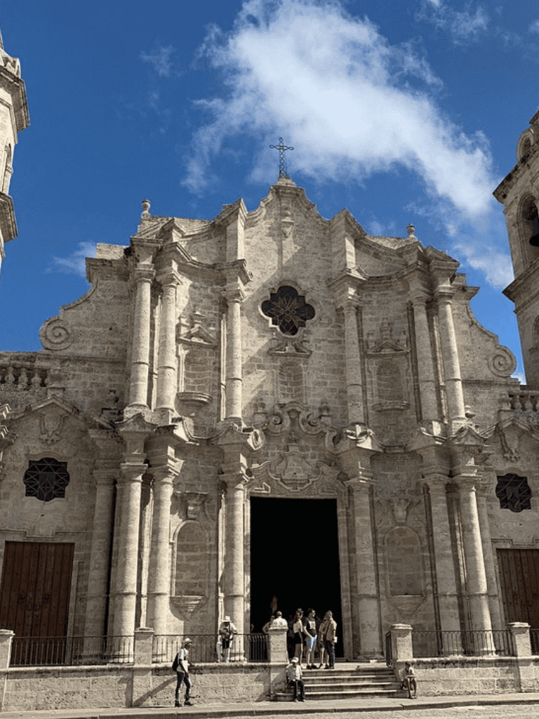 Intricate historic church with Baroque architecture and visitors outside under a blue sky.