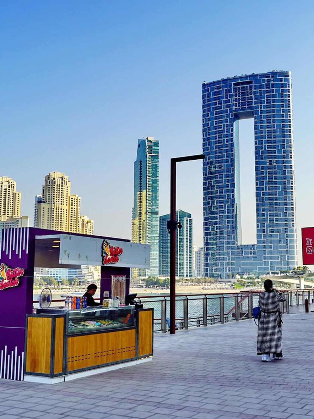 Vibrant cityscape featuring modern skyscrapers and a waterfront promenade with food vendors and pedestrian views in Dubai.