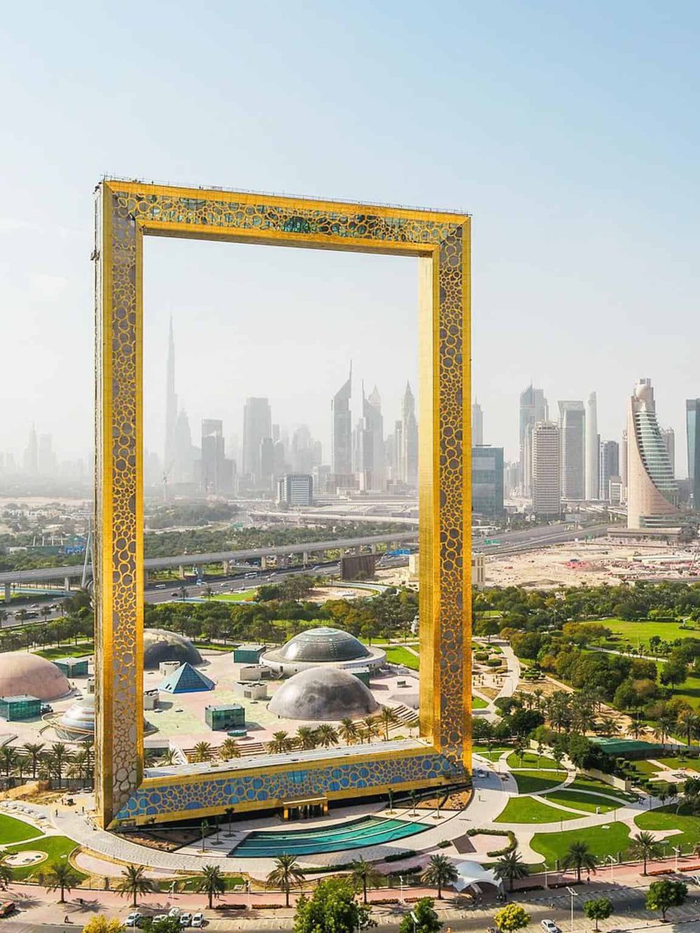 Golden frame installation in Dubai with city skyline view, modern architecture, and lush green park nearby.