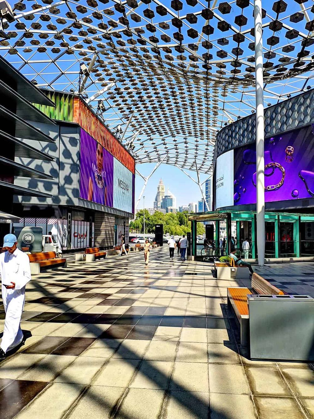 Modern outdoor shopping and entertainment pavilion with digital billboards and a distinctive patterned canopy.
