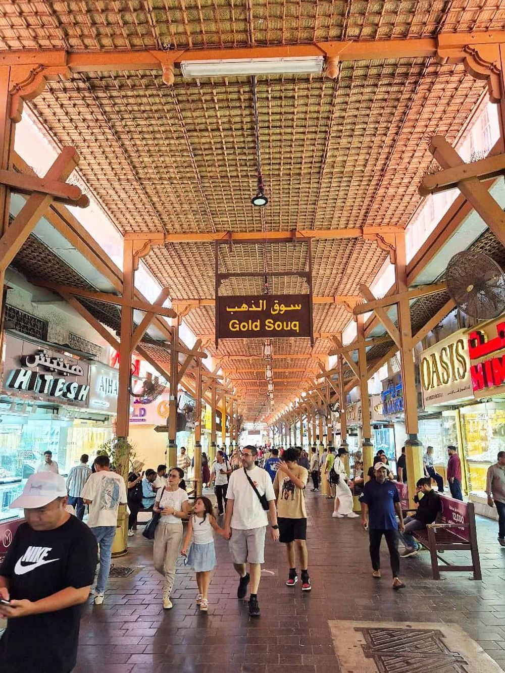 Bright indoor marketplace with signage in Arabic and English, bustling with shoppers and vibrant store displays.