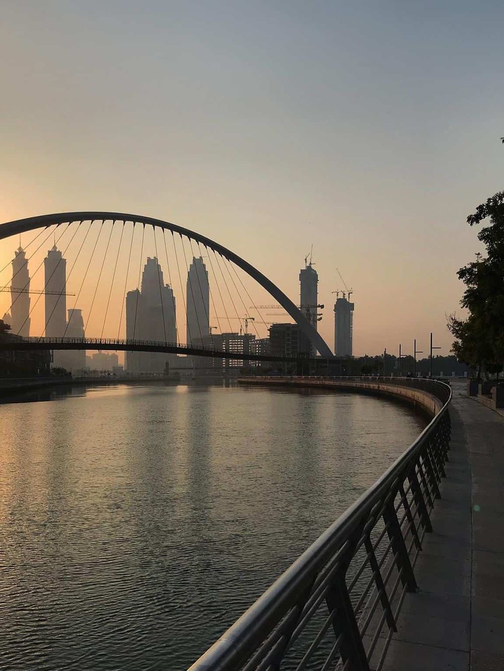 Modern city skyline with a distinctive arched bridge over a river at sunset, highlighting urban exploration and travel navigation.